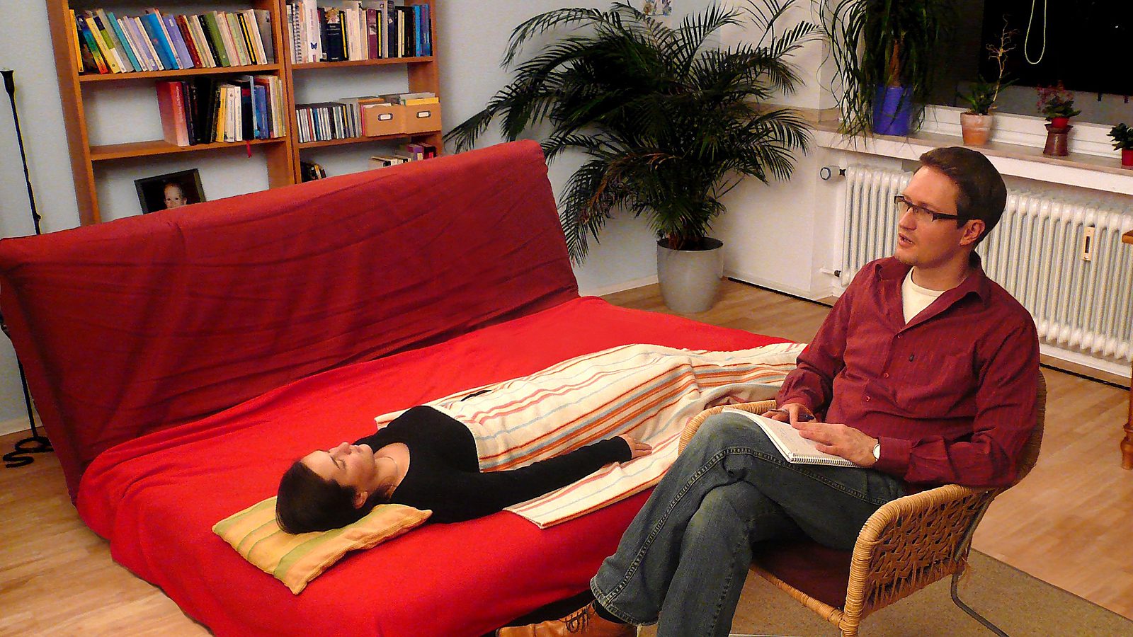 Hypnotherapeutische Sitzung: eine Klientin liegt entspannt auf der Liege, Jürgen Graf sitzt daneben und begleitet den Prozess